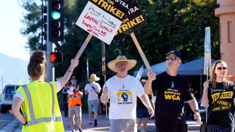 Striking actors tap signs together on a picket line outside Walt Disney Studios, Friday, Oct....