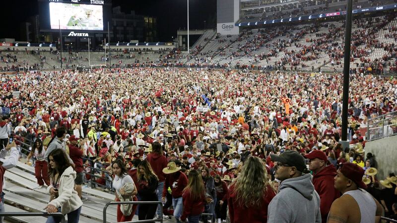 Washington State fans and players celebrate on the field after the team won an NCAA college...