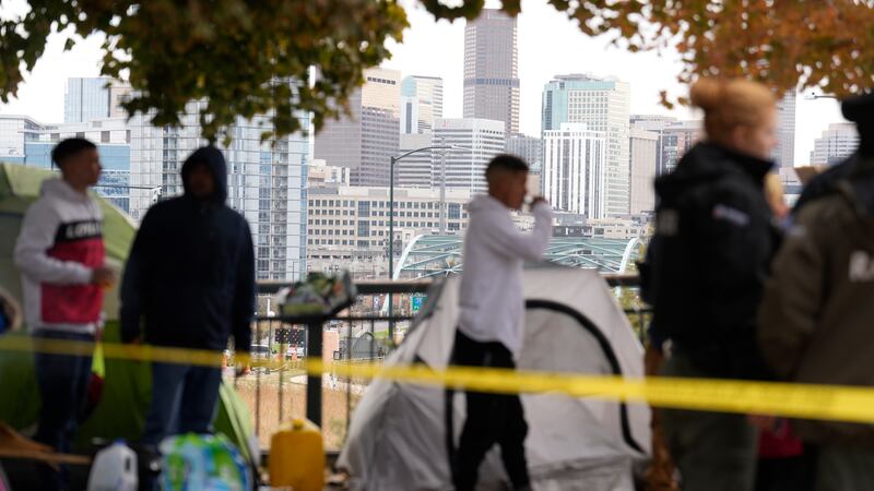 Occupants wait to see how police officers work during a city-sponsored sweep of an encampment...